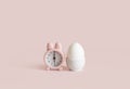 Easter time concept. Pink bunny clock and white chicken egg on pink background. Healthy food and breakfast concept. Space for text Royalty Free Stock Photo