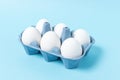 Easter white eggs in carton tray on blue background. Minimal concept