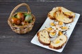 Easter wicker basket with colored eggs and sliced Easter bread in white plate on grey wooden board. Royalty Free Stock Photo