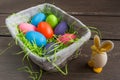 Easter wicker basket with colored eggs and a small egg rabbit on grey wooden board. Royalty Free Stock Photo