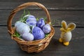 Easter wicker basket with colored eggs and a small egg rabbit on grey wooden board. Royalty Free Stock Photo