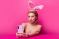 Easter woman with rabbit ears having video-call holding smart phone in hand shooting selfie on front camera. Royalty Free Stock Photo