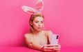 Easter woman with rabbit ears having video-call holding smart phone in hand shooting selfie on front camera. Royalty Free Stock Photo