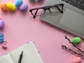 Work desk with devices and easter holiday multicolored eggs on pink background Royalty Free Stock Photo
