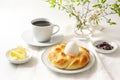 Easter yeast bread plaited in nest form with an egg, coffee, butter and jam as a festive Sunday breakfast on a white table, copy