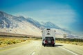 Camper towing Jeep drives on curving highway with Sierra Nevada mountains in background in