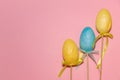 Eastern eggs with ribbon on stick, yellow, blue on pink background