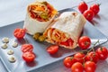 Eastern sandwich or healthy lavash snack with fresh vegetables and sauce on the gray plate decotated with cherry tomatoes, basil