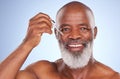 Easy application. Studio portrait of a mature man applying serum to his face against a blue background. Royalty Free Stock Photo