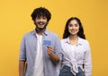 Easy contactless payments. Happy indian couple with credit card smiling at camera, posing over yellow studio background