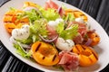 Easy dietary salad with mozzarella, prosciutto, grilled apricots, red onion and lettuce close-up on a plate. horizontal