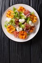 Easy dietary salad with mozzarella, prosciutto, grilled apricots, red onion and lettuce close-up on a plate. Vertical top view