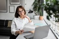 Easy paperwork. Happy female financial advisor using laptop and holding papers, working in cozy office and smiling Royalty Free Stock Photo