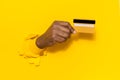 Easy payment. African american male hand holding plastic credit card, breaking through yellow paper sheet, closeup