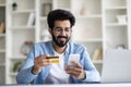 Easy Payments. Smiling Indian Man using Smartphone And Credit Card At Home Royalty Free Stock Photo