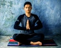 Easy Pose or Sukhasana is performed by a young man doing on the colorful mat wearing black attire. Royalty Free Stock Photo