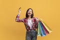 Easy shopping. Overjoyed asian woman holding credit card and bright shopper bags, got cashback bonus, yellow background