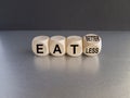 Eat better or less symbol. Turned a cube and changed words eat less to eat better. Beautiful black background. Grey table.