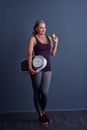 Eat right and exercise. Studio portrait of an attractive mature woman holding an apple and a weightscale against a blue Royalty Free Stock Photo