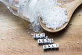 Eat less salt message written near wooden spoon full of granulated salt and shaker on rustic background