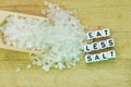 Eat less salt recommendation with plastic letters and granulated salt on wooden chopping board