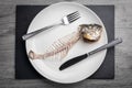 Eaten fish skeleton on the white plate on gray wooden table. Concept for food shortage and misery. Top view