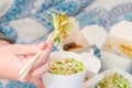 Eating Chinese take away food with chop sticks at home with bed sheets in the background. Spicy asian food in white box - salad,