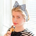 Eating chocolate beautiful blond pinup girl with red lips and green eyes gently smiling looking at camera over sun lighted blinds Royalty Free Stock Photo