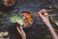 Eating delicious asian bowl with rice noodles, vegetables and to