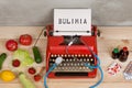 Eating disorder concept - typewriter with text Bulimia, stethoscope, vegetables, fruits and berries, tablets and pills