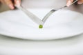 Eating disorder. Girl is holding a plate and trying to put a pea