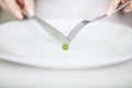 Eating disorder. Girl is holding a plate and trying to put a pea