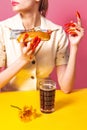 Food pop art photography. Young woman tasting hot dog with dark beer isolated on bright pink and yellow background Royalty Free Stock Photo