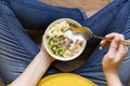 Eating healthy breakfast bowl. Yogurt, buckwheat, seeds, fresh fruits in white bowl in woman`s hands. Clean eating, dieting, detox