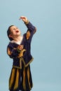 Eating jelly candies. Happy little boy in costume of medieval pageboy, little prince over light blue background. Concept