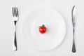 Eating a low calorie diet concept. Top above overhead flat-lay view photo of a plate with a single tomato with fork and knife Royalty Free Stock Photo