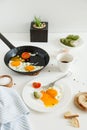 Eating in the process, fried eggs in a frying pan and on a plate, toast with avocado and a cup of coffee for breakfast. Royalty Free Stock Photo