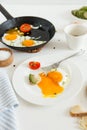 Eating in the process, fried eggs in a frying pan and on a plate, toast with avocado and a cup of coffee for breakfast. Royalty Free Stock Photo
