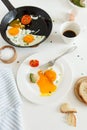 Eating in the process, fried eggs in a frying pan and on a plate, toast with avocado and a cup of coffee for breakfast. Royalty Free Stock Photo