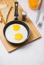 Eating in the process, fried eggs in a frying pan, toast and orange juice for breakfast on a white background. Daylight Royalty Free Stock Photo