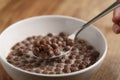 Eating with spoon chocolate cereal balls with milk in white bowl for breakfast on wooden table Royalty Free Stock Photo