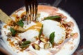 Eating Turkish poached eggs or Cilbir on a bed of light yoghurt topped with chilli oil, pistachios and mint leaves Royalty Free Stock Photo