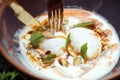 Eating Turkish poached eggs or Cilbir on a bed of light yoghurt topped with chilli oil, pistachios and mint leaves. Royalty Free Stock Photo