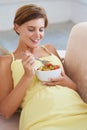 Eating for two. A relaxed pregnant woman enjoying a healthy salad while sitting on the couch. Royalty Free Stock Photo