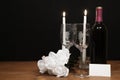 Eautiful etched wine glasses and bottle of red wine, white candles and white roses on wooden table with name tag on dark Royalty Free Stock Photo