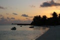 Eautiful sunset in the Maldives. White sand, calm ocean, people coming out of the water, orange sky with clouds