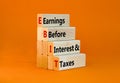 EBIT symbol. Concept words EBIT earnings before interest and taxes on wooden block on beautiful orange background. Businessman