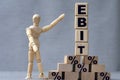 EBIT , the word is on cubes on a gray background, next to it is a wooden man