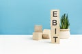 ebit - word is written on wooden cubes on a blue background. close-up of wooden elements. in the background is a green