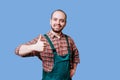 An ebullient young farmer with a beard is photographed in overalls, giving a thumb up